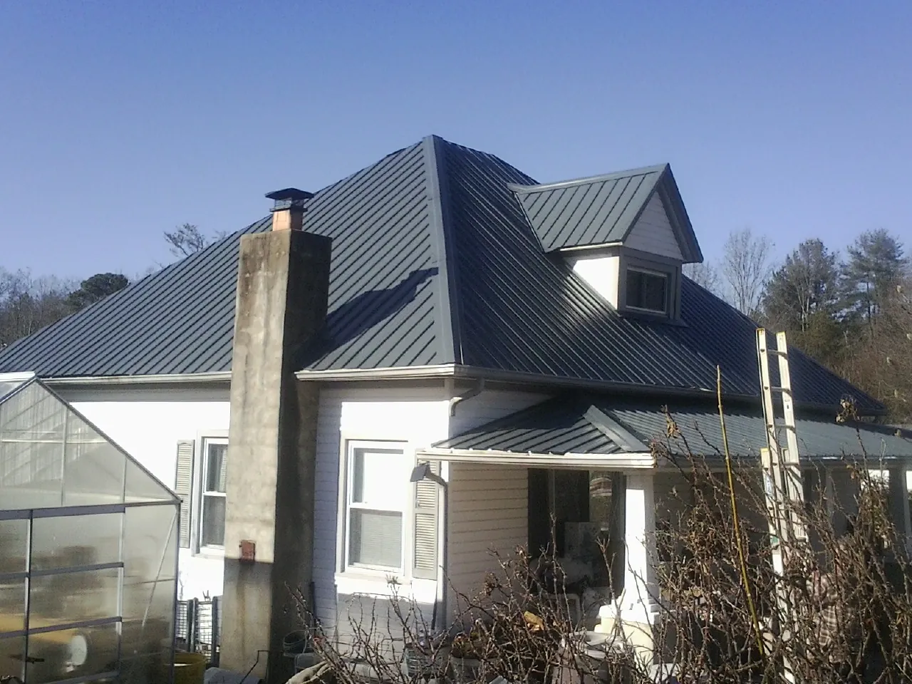 Dark blue standing seam metal roof on a white farmhouse with dormer — Slate & Tile Roof Repair by Roofing Brothers in Argos