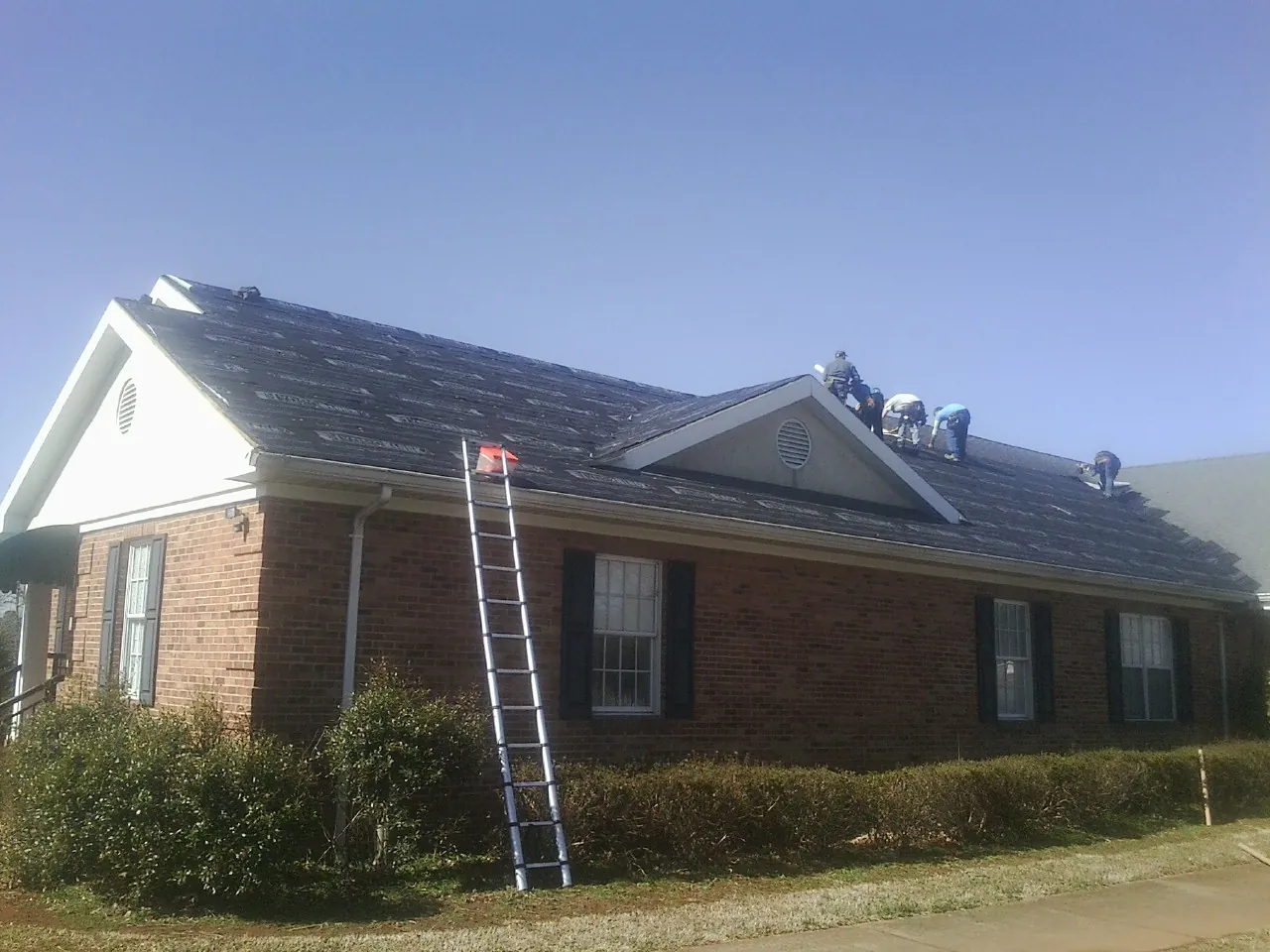 Crew tearing shingles off a brick ranch roof with a ladder set — Emergency Roof Repair work by our crew in Argos