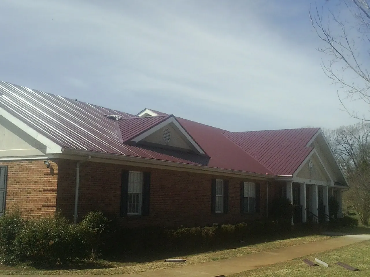 Red metal roof with gabled entries on a long brick building, from a Hail Damage Roof Repair job in Argos