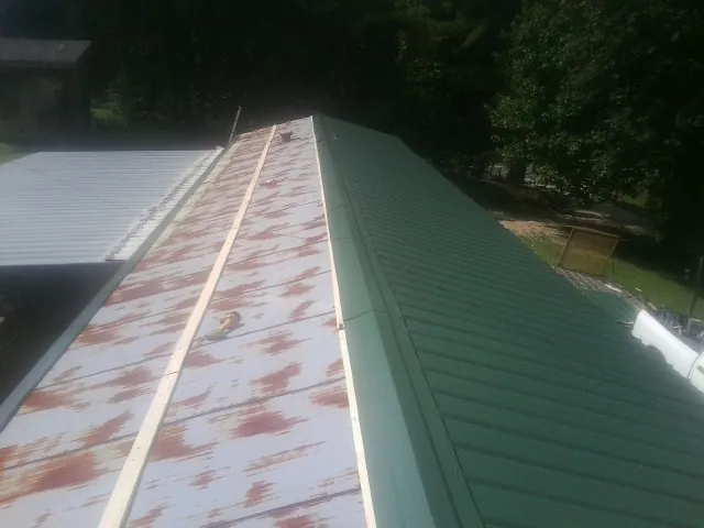 Old rusted panels beside newly installed green metal roofing — Wind Damage Roof Repair by Roofing Brothers in Argos