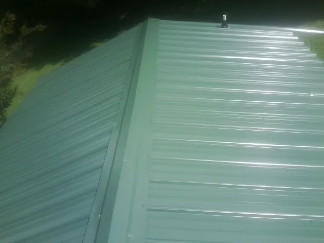 New green metal panels meeting at the ridge of a roof — Flat Roof Repair work by our crew in Argos