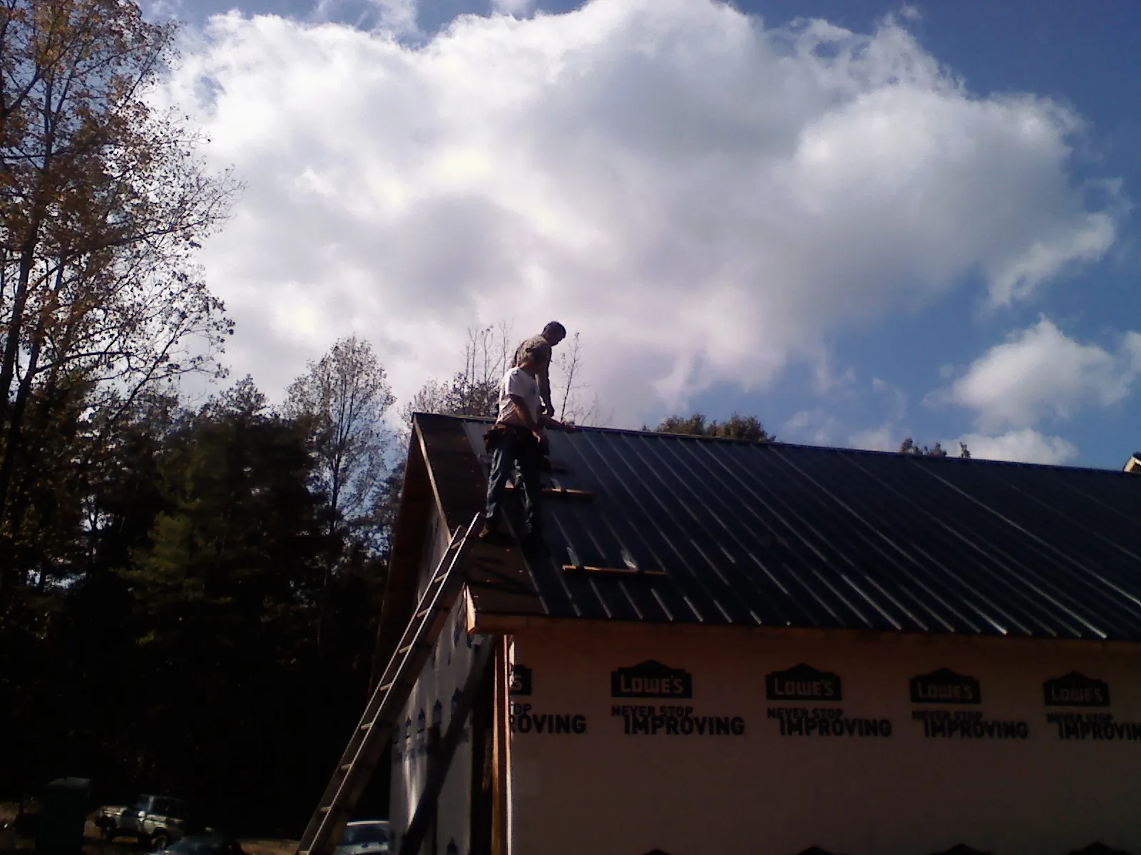 Roofer fastening dark metal panels high against a cloudy sky, from a Roof Inspection job in Argos